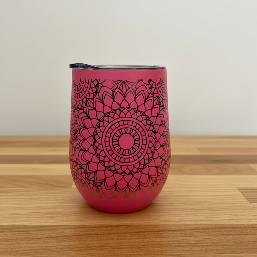 Pink tumbler with black mandala design on a wooden surface